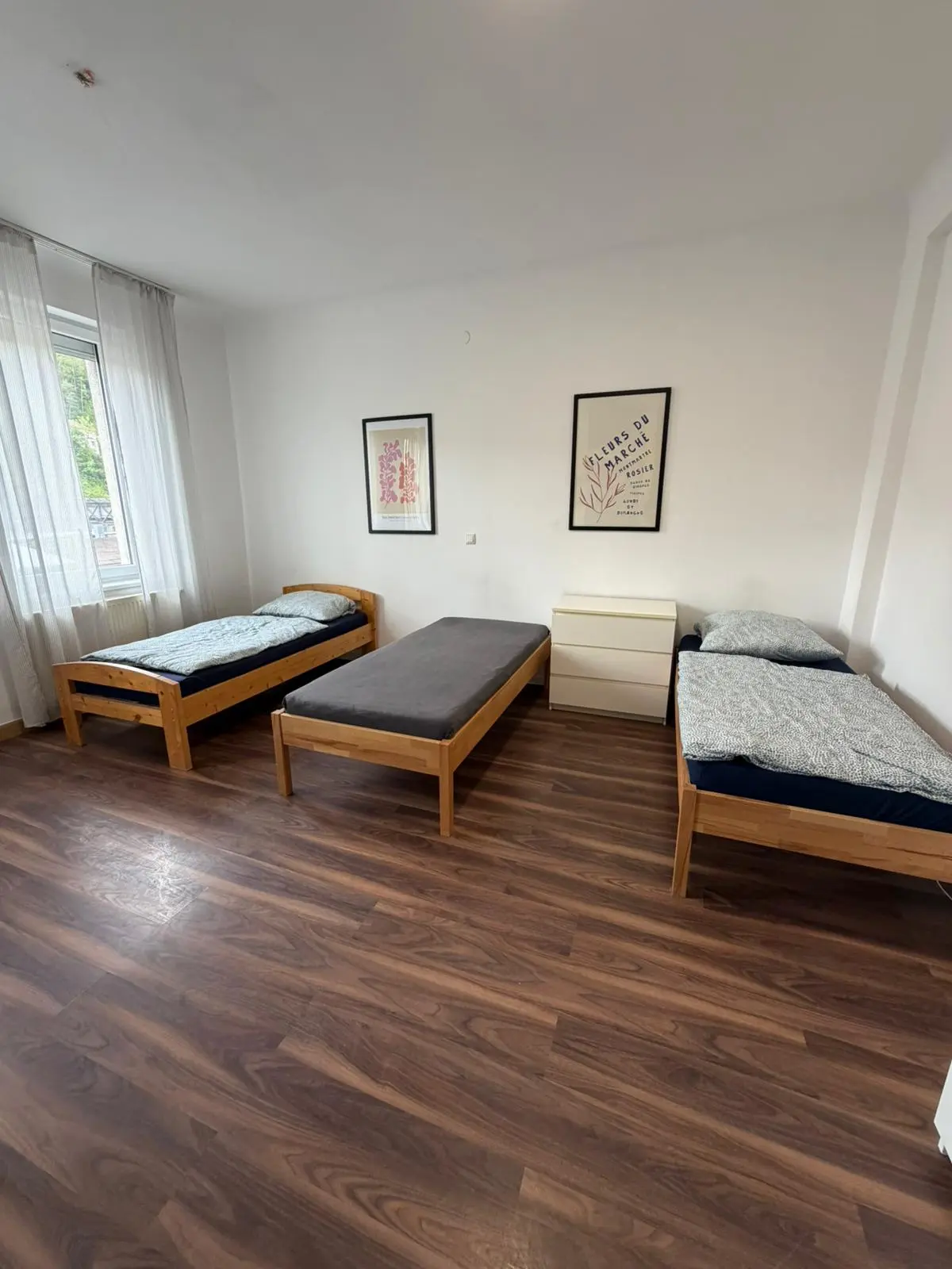 Helles Schlafzimmer einer Monteurwohnung in Geislingen mit drei gemütlichen Einzelbetten und Kommode.