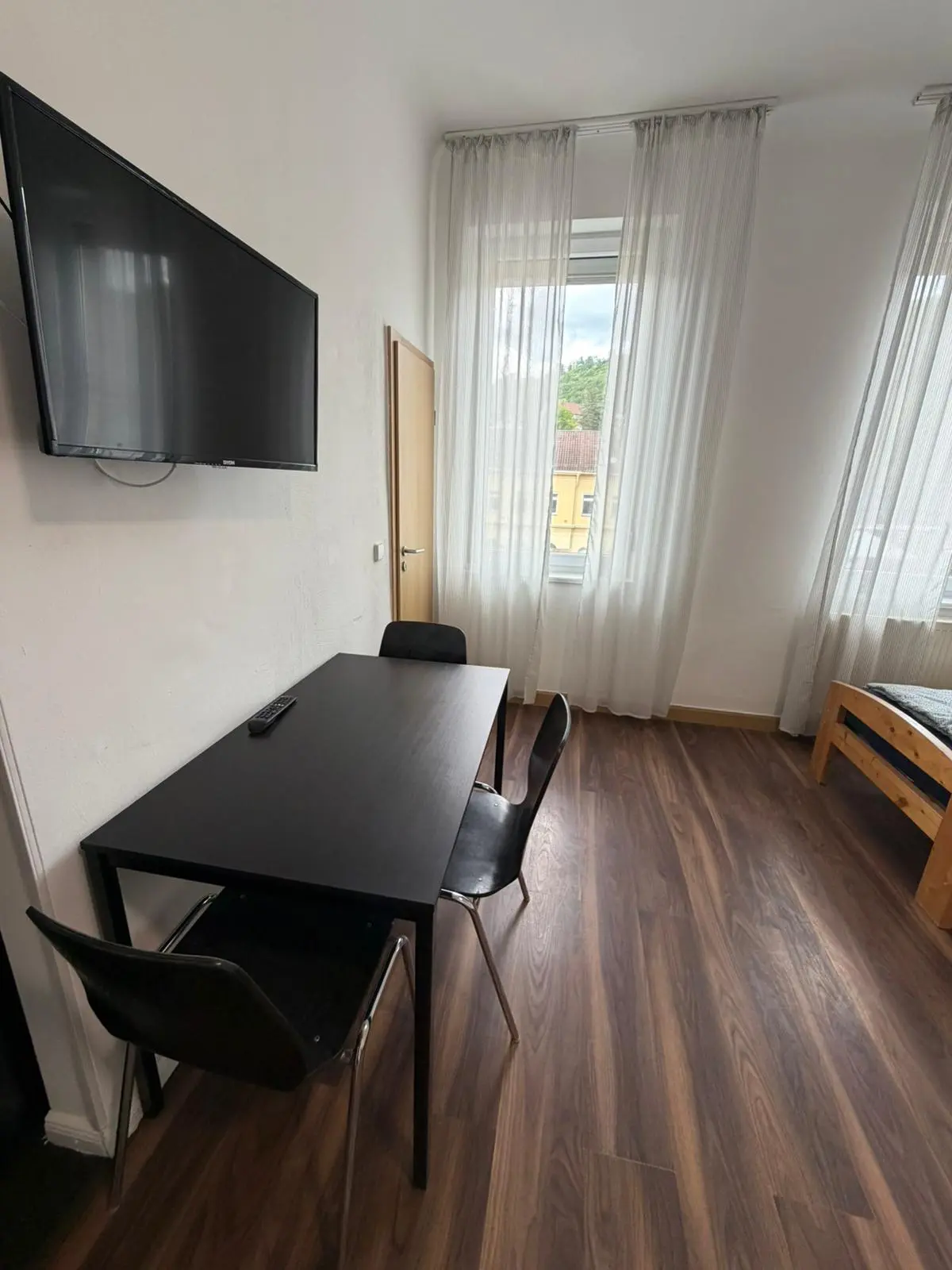 Esstisch mit Stühlen und an der Wand montiertem Fernseher in einer Monteurwohnung in Geislingen.