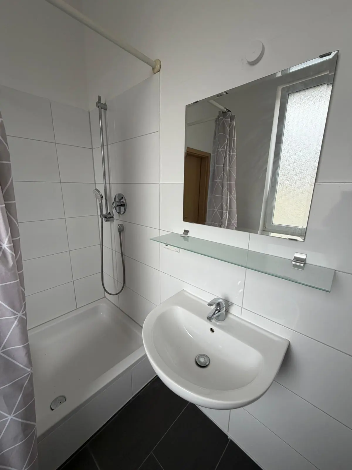 Modernes, weiß gefliestes Badezimmer mit Waschbecken und Spiegel in der Handwerker-Unterkunft Geislingen.