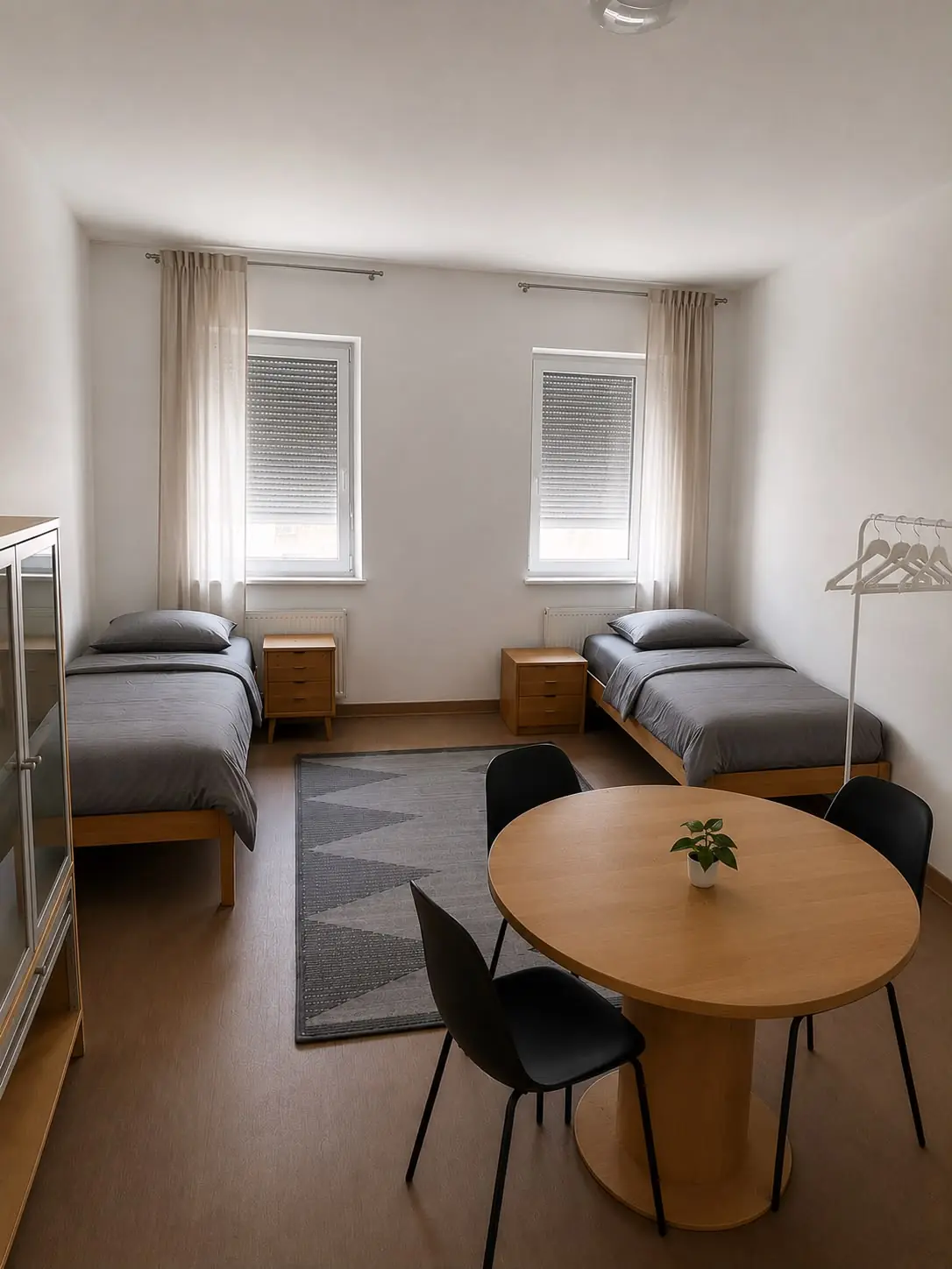 Helles Zweibettzimmer mit Betten, Tisch, Stühlen und Fensterfront in Unterkunft auf Zeit