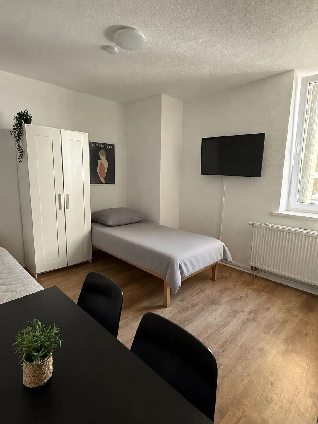 Komfortables Monteurzimmer mit Einzelbett, modernem Flachbild-TV an der Wand und Esstisch mit Stühlen.