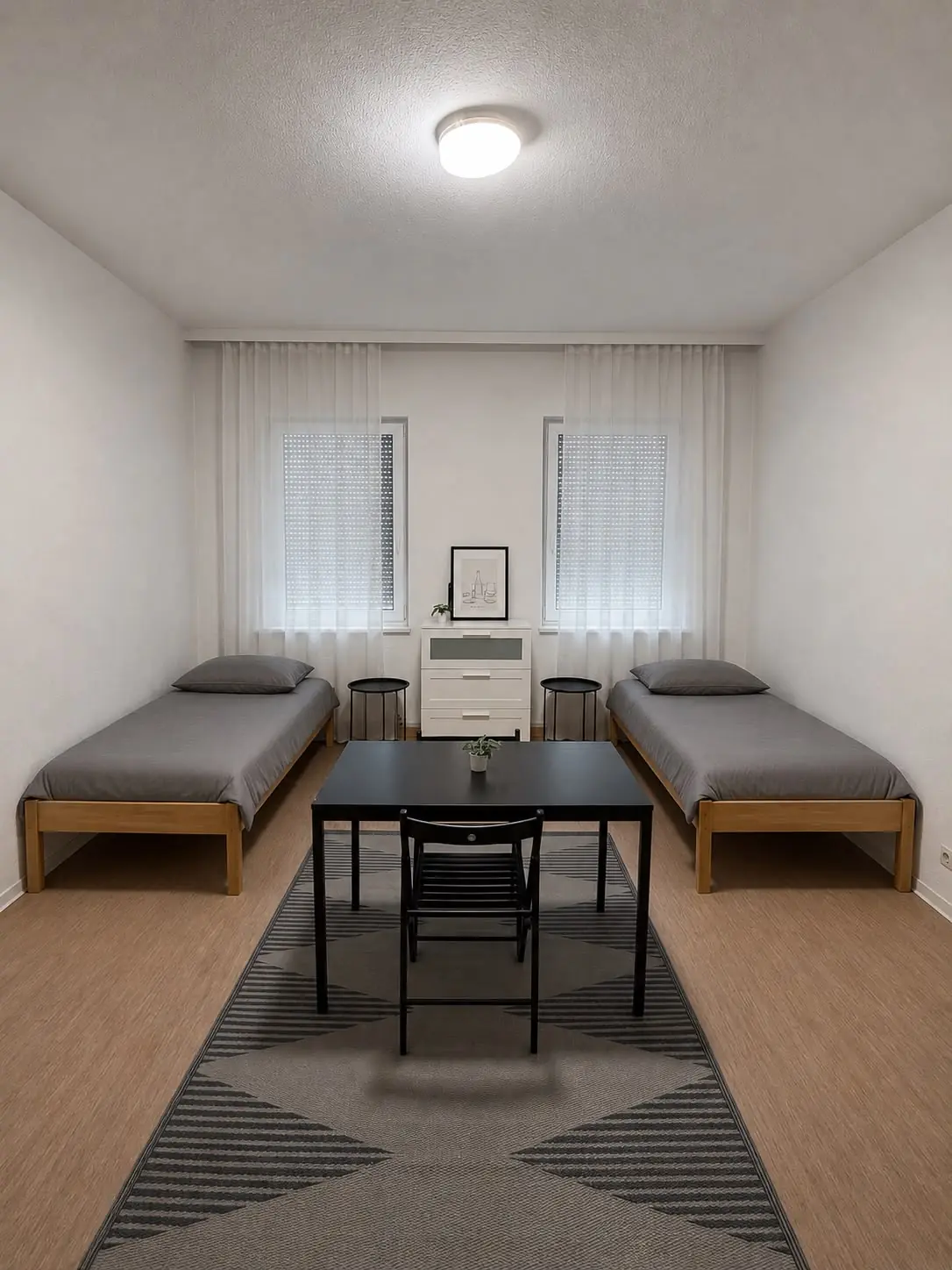 Möbliertes Zweibettzimmer mit Tisch, Stühlen und zwei Betten in heller Unterkunft auf Zeit