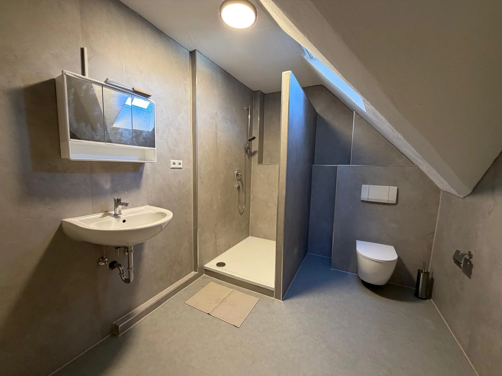 Großzügiges Dachgeschoss-Badezimmer in Grauoptik mit begehbarer Walk-In-Dusche, WC und Spiegelschrank.