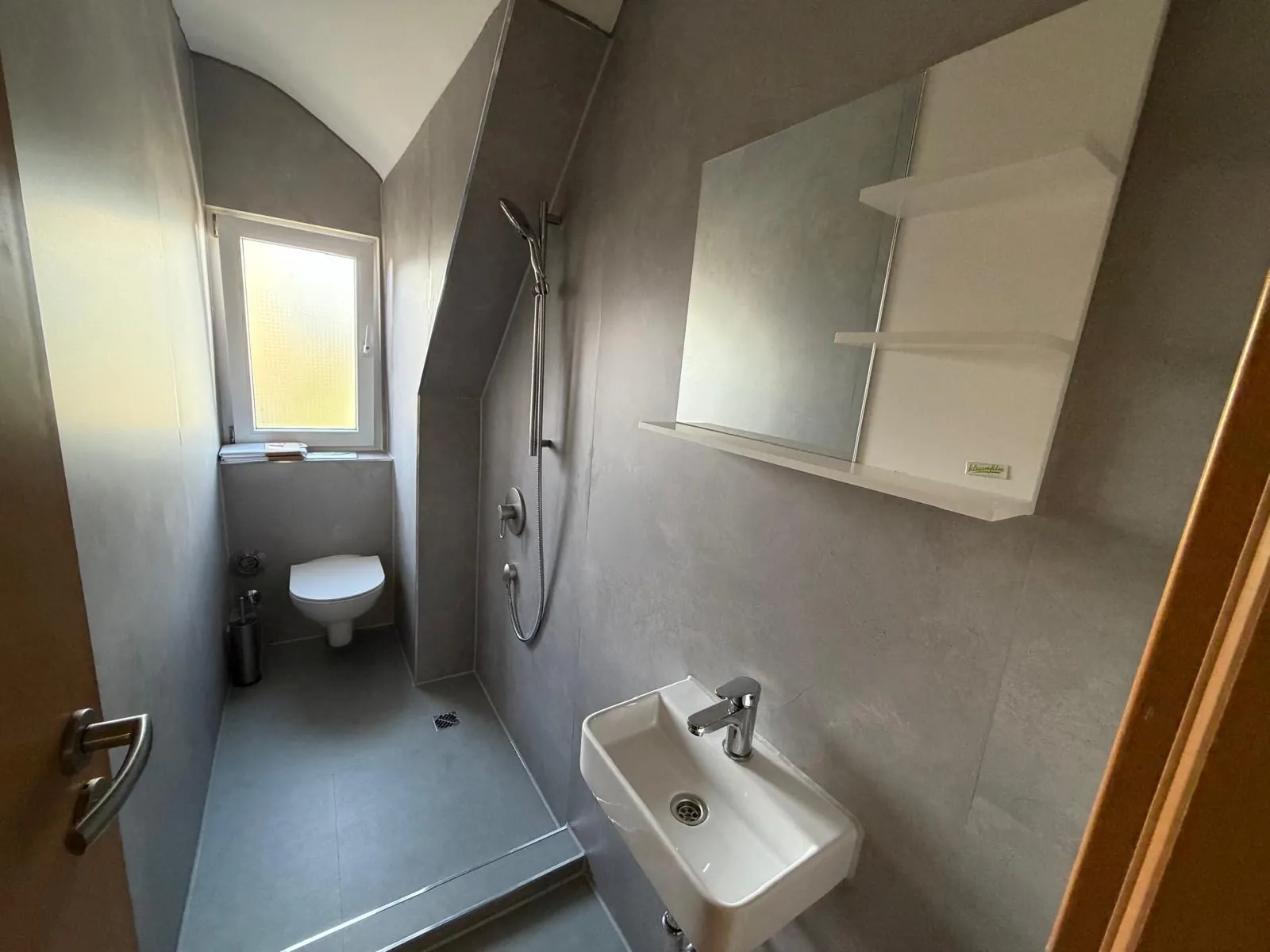 Schmaler, modern in Grau gefliester Sanitärraum mit bodengleicher Dusche, WC und Waschbecken.